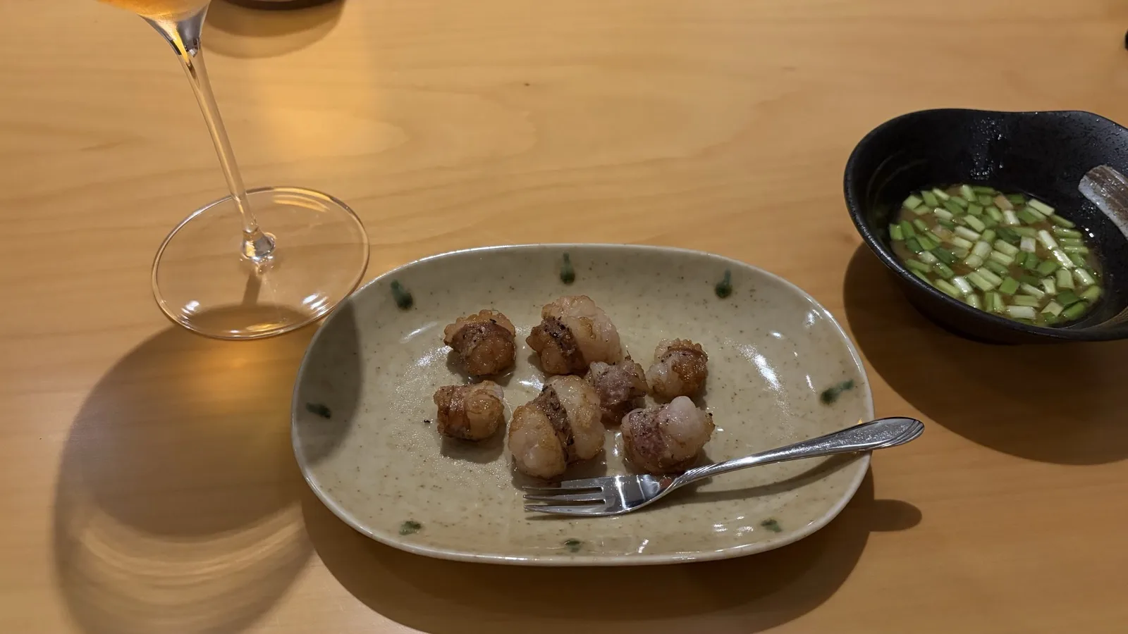 ワイングラスとホタテの焼き物、薬味の小鉢を囲むテーブルのイメージ